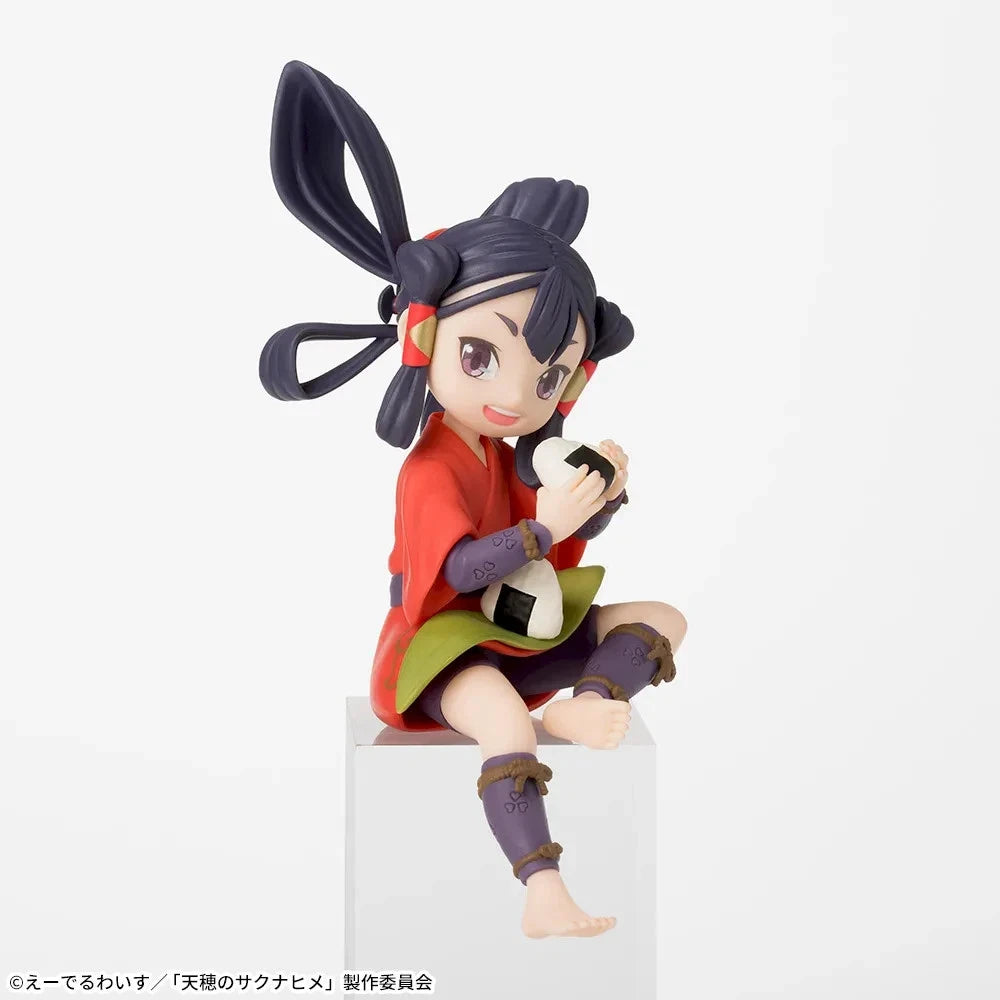 A collectible anime figurine of a girl with dark hair in a high ponytail sitting on a white pedestal, wearing a red top, green skirt, and holding a black-and-white ball. The photo is taken against a clean white background.