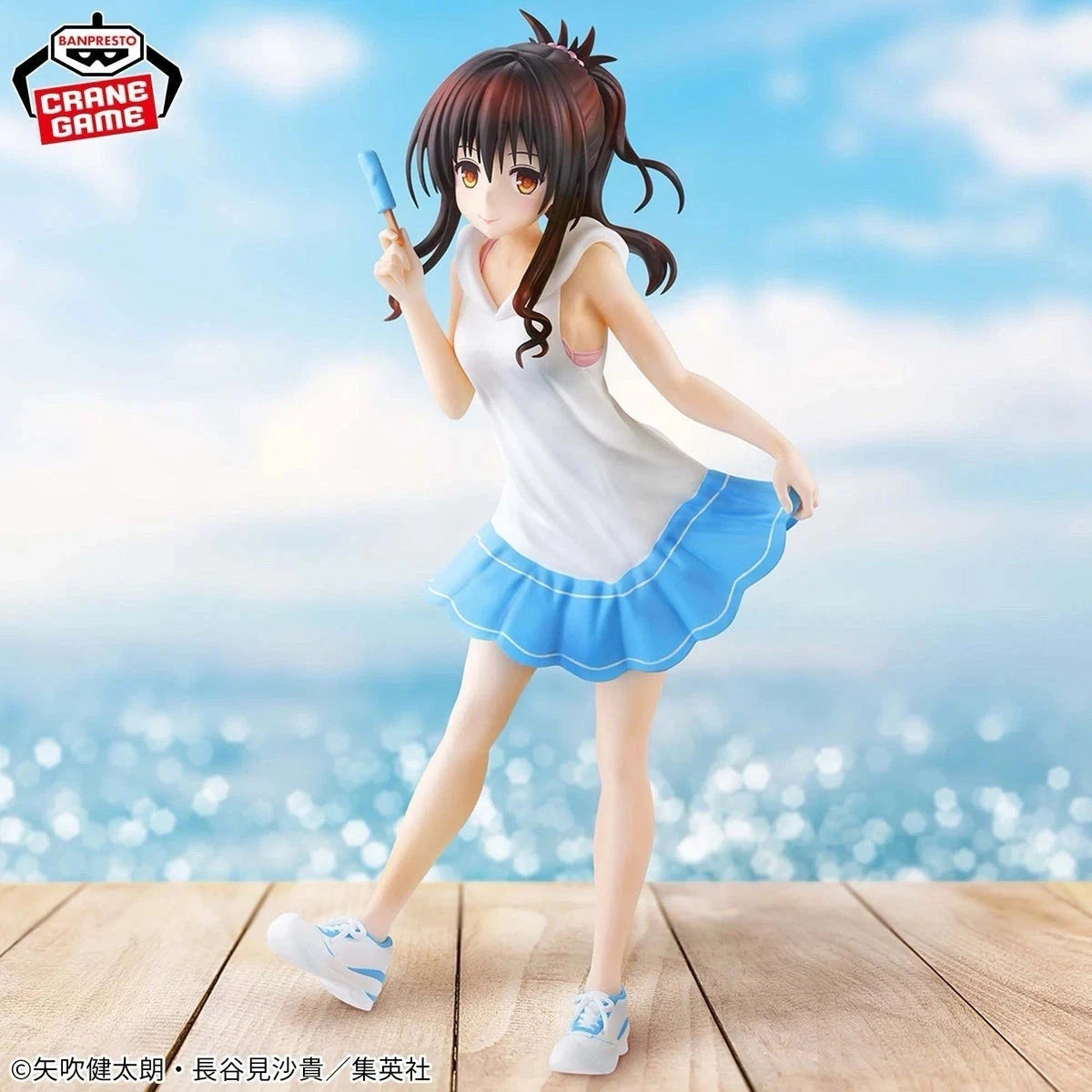 Anime character figurine in a white top and blue skirt against a blurred beach background