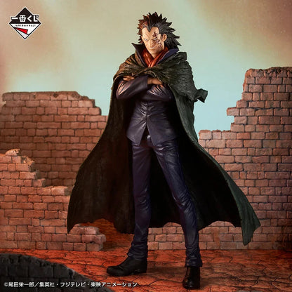 A collectible action figure/statue of a spiky-haired male character in a dark coat and black outfit, posed with arms crossed in front of a ruined brick wall backdrop. The figure is shown against a stylized painted background with a logo in the top-left corner.